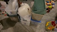 Multiple plastic storage containers stacked, including clear, beige, and green bins. Roll of bubble wrap placed on top.