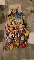 Top-down view showing an extensive assortment of over 50 stuffed animals including recognizable characters from various franchises arranged neatly on the floor and in a bin.