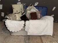 Plastic bin containing folded table linens including lace, embroidered, crocheted, and other materials.