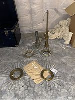 Photo showing multiple separate pieces of the chandelier, including brass circular bases with attached clear crystal rods and loose crystal pieces laid out on a concrete floor.
