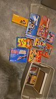 Photo showing multiple vintage Playmobil boxed sets, Mr. Potato Head products, and classic board games including Tic Tac Teddy and Shake Bingo, arranged on floor and in storage bin.