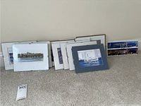 Group of 14 photographic wall art prints arranged on floor, framed with mats, showing seascapes and cityscapes.