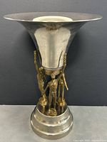 Front view of the trophy showing the triumphant men figures holding the silver-tone cup on a tiered base.