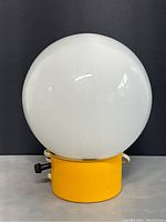 Front view of white opaque glass globe lamp shade on yellow cylindrical base with attached power cord and knob switch.