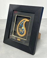 Framed 24K gold plated Persian paisley motif artwork showing detailed gold and blue design in black shadow box frame with gold inner edge.