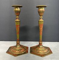 Pair of vintage etched solid brass candlesticks with intricate hand painted details in reds and greens, showing the full front view with hexagonal bases.