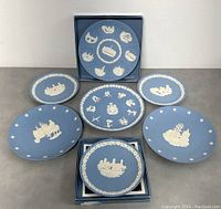 Seven Wedgwood blue jasperware collector plates arranged on surface with two plates in original Wedgwood boxes.