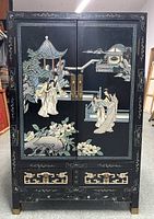Front view of black lacquer cabinet with mother of pearl inlay showing detailed scenes of figures, pagodas, and flora on the doors and drawers.