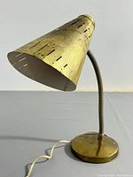 Side view of the brass desk lamp showing cone-shaped perforated shade and flexible gooseneck stem on round base with attached power cord.