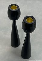 Pair of sleek black wooden candleholders with brass inserts seen from angled top-down view on gray surface.