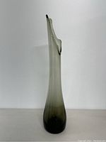 Front view of the tall, slender smoke gray glass vase showing the swung irregular top edge against a plain background.