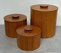 Front view of three nested teak containers with lids on, showing size differences and wood grain