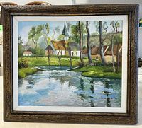 Framed painting showing village landscape with water reflection and village church steeple.