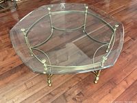 Octagonal glass top coffee table showing yellow brass stand and glass surface on wooden floor.