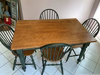 Photo of wooden dining table with natural wood finish top and green painted legs with four matching green spindle back chairs around it.