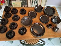 Full view of the dinnerware set showing plates, bowls, cups, saucers, creamer, and sugar bowl all in matching black with bronze geometric pattern.