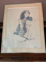 Framed grayscale art print showing a woman seated with curly hair and casual clothing, in a metal frame with cream mat.
