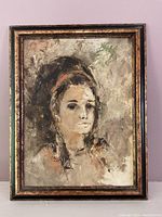 Full view of framed abstract portrait painting of a woman against a light purple wall.