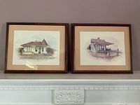 Pair of framed art prints featuring rural train stations with brown wooden frames and tan mats.