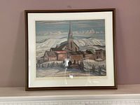 Framed artwork titled 'Church Of St. Urbain' showing a church with a tall steeple in a snowy landscape, with visible scratches and dust on the wooden frame.