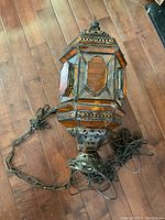 Photo of a hexagonal hanging light fixture with metal frame and colored glass panels, showing the full fixture and chain on a wooden floor.