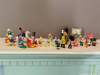 Front view of all miniature figurines arranged in a line on a white shelf against grey wall.