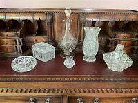 Wide view showing entire set of 5 crystal and glassware items on wooden surface with small cabinet backdrop