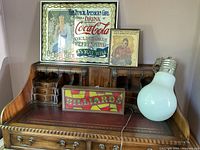 Photo showing all items on a wooden desk: Coca-Cola sign, framed print, Billiards light-up sign (off), and novelty light bulb lamp