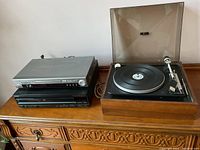 Photo showing the full lot of vintage electronics: ELAC turntable on the right with wood base and dust cover, stacked silver Samsung DVD player and black device on the left on the dresser.