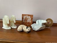 Photo showing all six figurines on wooden surface including seahorses, cat, polar bear, fossil, and carved tile
