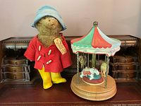 Paddington Bear next to carousel music box on wooden surface, showing overall size and condition