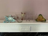Full view showing all glass items including multi-colored decorative piece, two clear floral bowls, six small clear glass vessels, and large green-amber tri-leaf bowl.