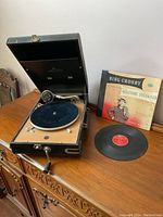 Decca Salon portable record player with lid open, showing tonearm, platter with blue felt mat, and crank handle. One Bing Crosby 'Welcome Stranger' vinyl record on the table next to the player with its cover.