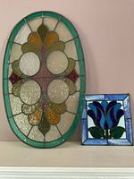 Two stained glass panels shown side by side: a large oval panel with abstract floral pattern and a smaller square panel with blue tulip design.