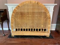 Front view of wicker rattan headboard showing arched top and woven cane panel with natural light brown color and some wear.