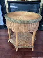 Round wicker table shown from a front angle with details of top weaving, legs, and lower shelf.