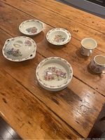 Overhead view of entire set with 4 bowls and 2 mugs arranged on wooden table, including one lidded bowl for warming food.