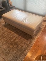 Full view of rectangular grey leather ottoman on carpet beside wooden floor