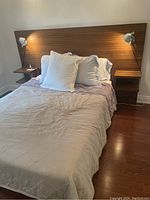 Full view of headboard mounted on wall with mattress, bedding and two lamps attached