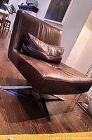 Full view of brown leather swivel chair on polished hardwood floor, showing seat, back and bolstered cushion