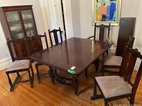 Full view of antique dark wood dining table with six matching chairs around it, showing wood floor and fixtures in background.
