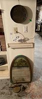 Rustic steel drum and mirror with wood frame hanging on wall, wall hook with bell and gong on floor beneath mirror
