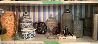 Shelf displaying various ceramic vases, jars, pitchers, glass trinket dish, and whiskey stones box