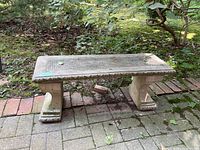 Full view of concrete bench outdoors on stone and moss-covered ground, showing rectangular top and sculpted supports
