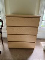 Front view of four-drawer IKEA dresser showing smooth light wood finish and handle grooves.