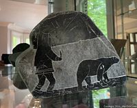 Front side of the stone carving showing a person and bear etched in black and white on stone.