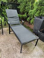 Side view of outdoor lounger showing black powder coated metal frame and black PVC fabric with visible armrest and leg wheels.