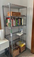 Full view of metal shelving unit containing wicker baskets, books, and a cleaning bottle (contents not included)