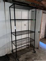 Full front view of the five shelf metal baker style rack with casters, showing all shelves and wheels on a concrete basement floor.