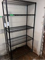 Full view of black metal bakers style shelving unit with five wire shelves installed, against a wall.